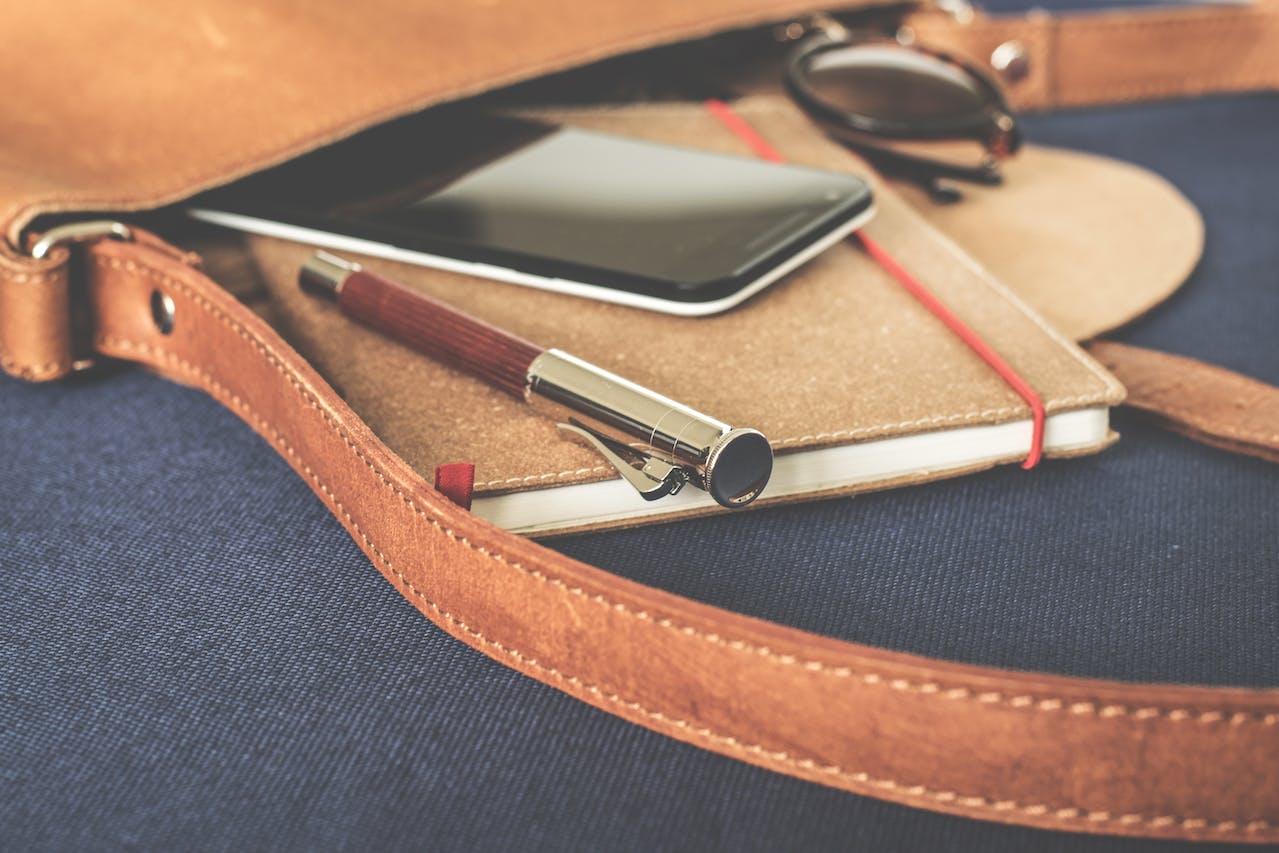 Smartphone Displaying Black Screen on Notebook Beside Pen and Sunglasses<br />
